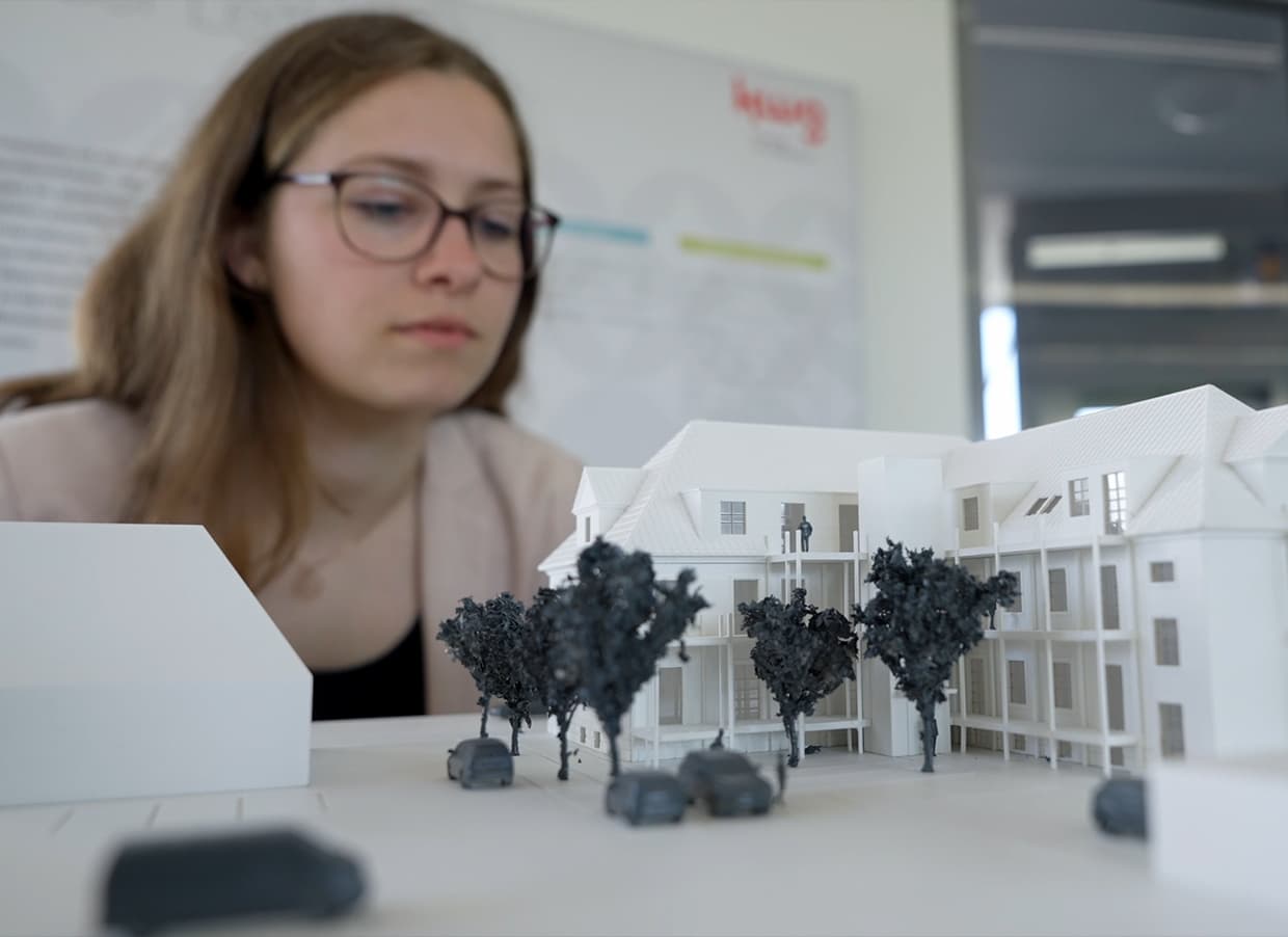 Foto einer kwg Mitarbeiterin und einem kleinen Modellhaus