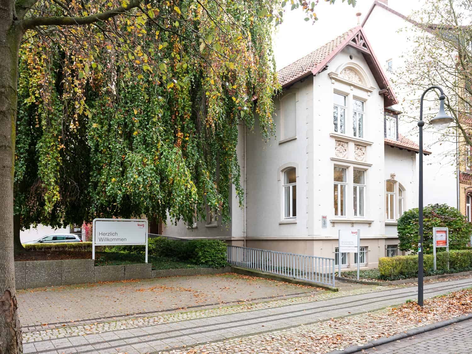 Ein Foto eines alten Gebäudes mit ein em grünen Baum im Vordergrund