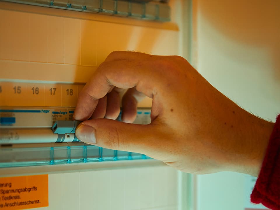 Eine Hand legt einen Schalter in einem Sicherungskasten um