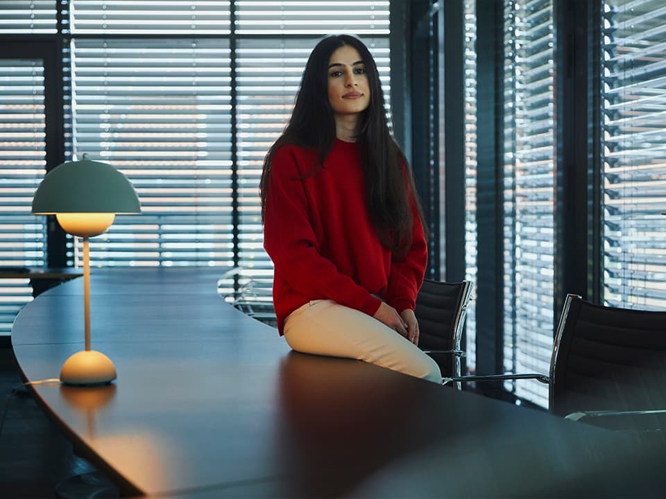 Eine junge Frau sitzt auf einem Schreibtisch in einem Büroraum