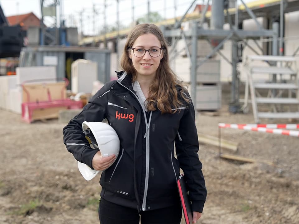 Eine weibliche Person in Baustellenkleidung, im Hintergrund eine Baustelle